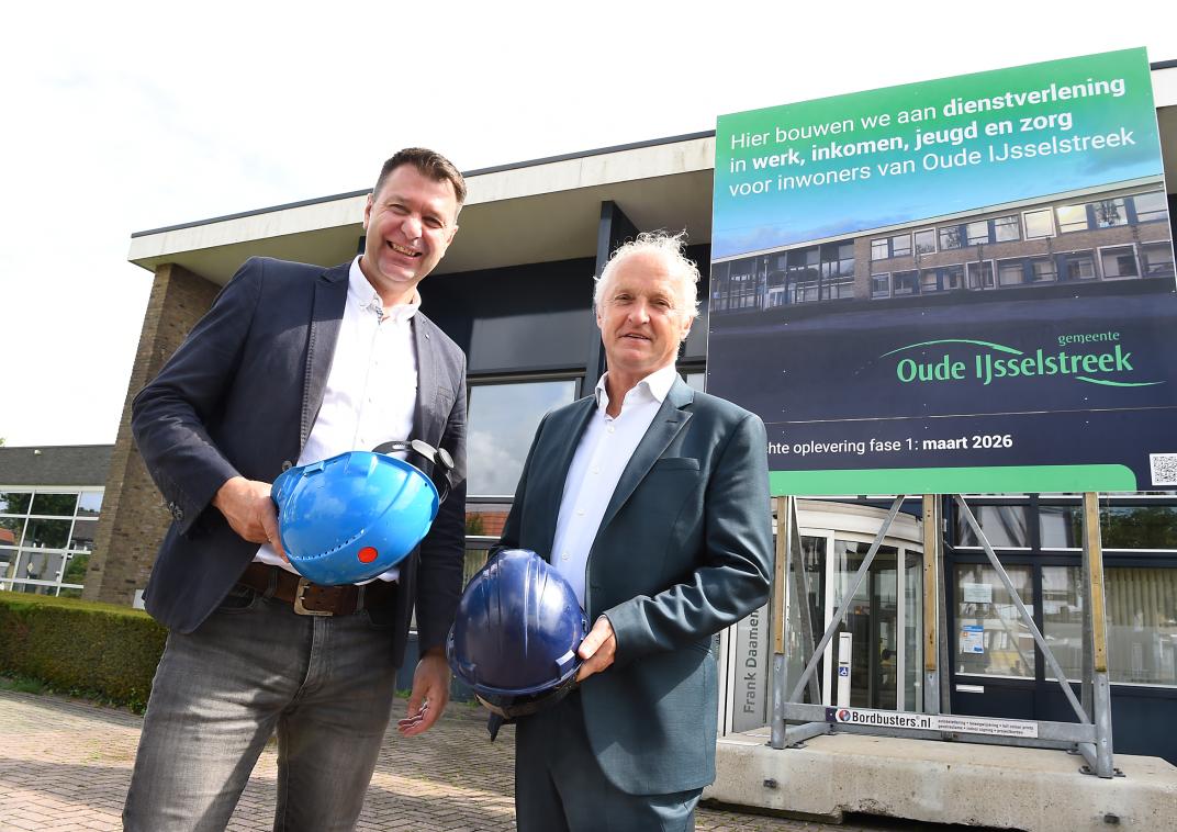 Wethouders Marco Bennink en John Haverdil voor het bouwbord bij het Frank Daamenpand