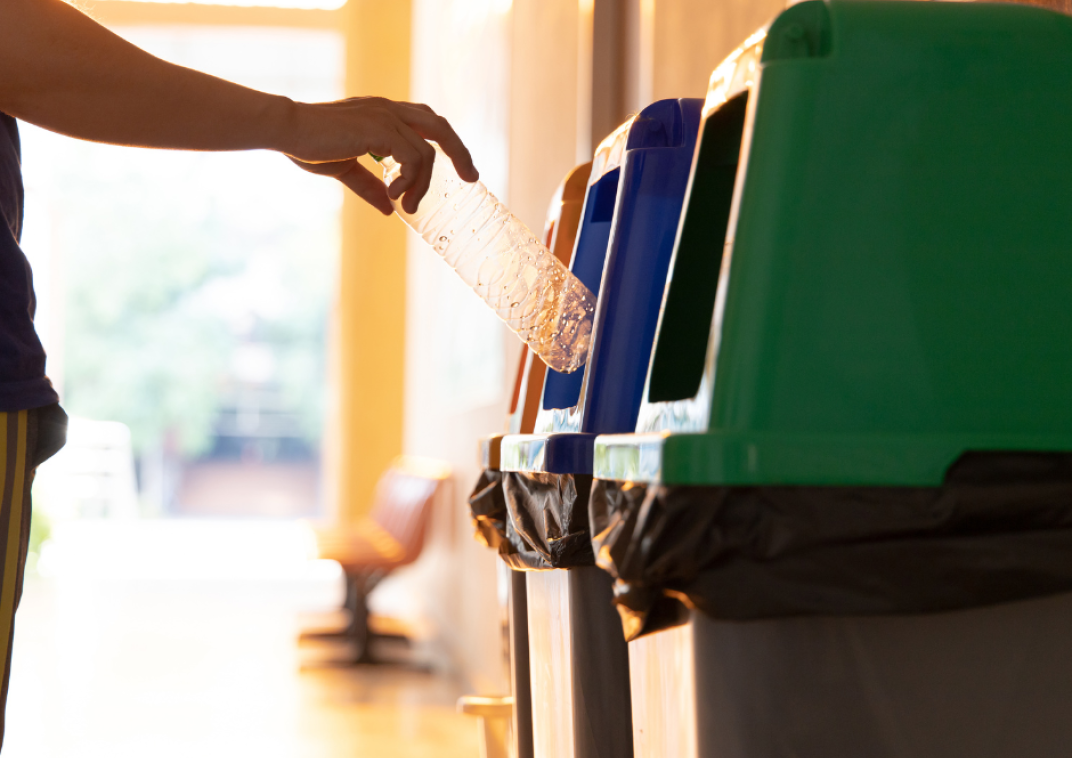 Afvalbakken om afval te scheiden met hand die een plastic fles in een plastic bak doet