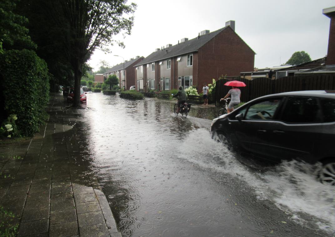 Een ondergelopen straat waar een auto doorheen rijdt.